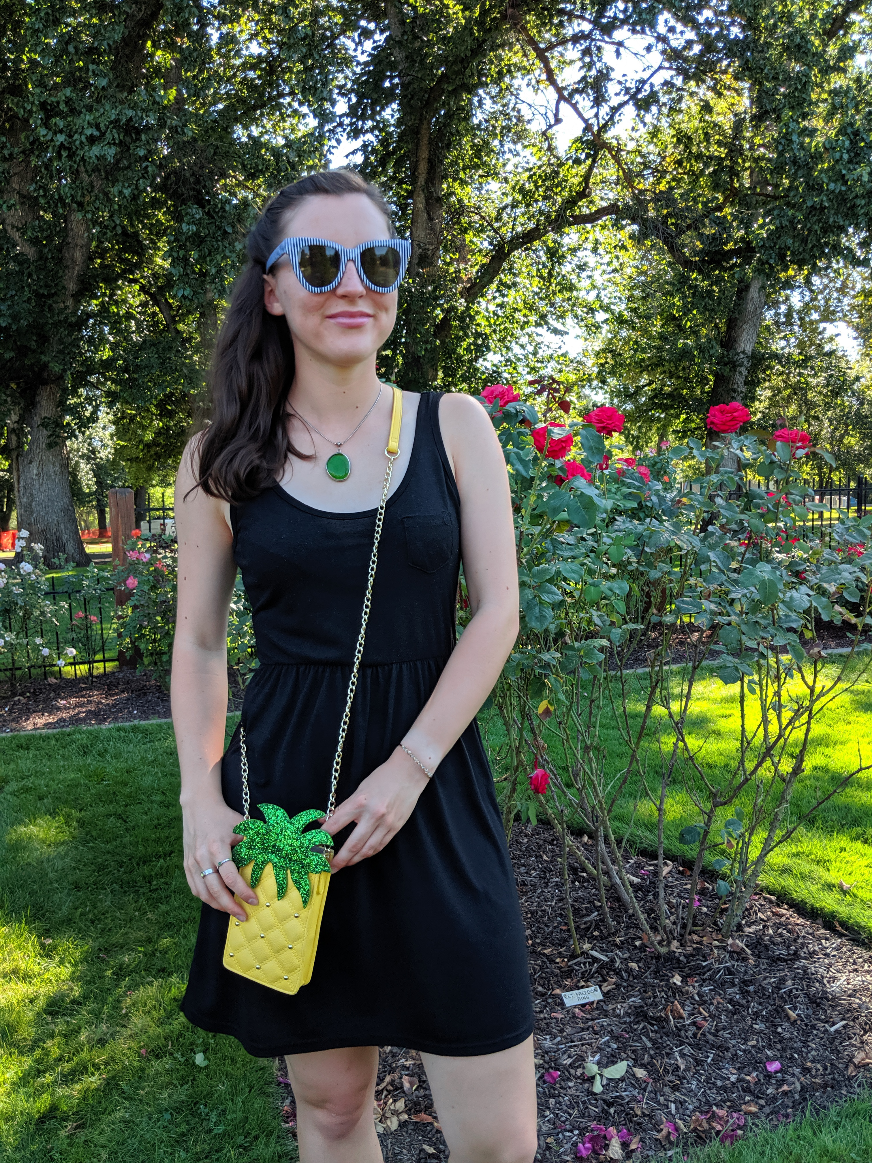 black dress, green accessories, striped sunglasses, pineapple purse